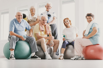 Low angle on smiling active elderly people on balls after physical classes in sport club