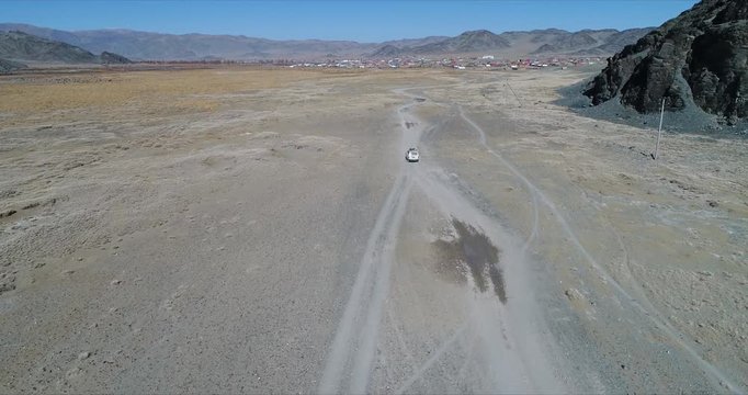 4k 60 fps Mongolia Aerial view of Altai desrt track with 4x4 driving - driving in plain with town in back