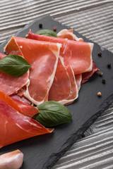 Italian prosciutto crudo or spanish jamon on a stone plate wooden background