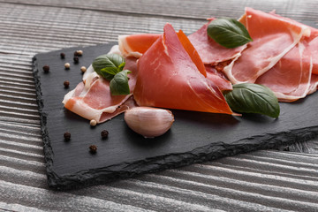 Italian prosciutto crudo or spanish jamon on a stone plate wooden background