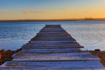 View from a wooden pier over a river towards the setting sun