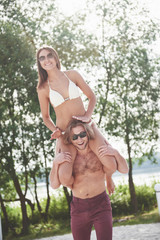Happy young man wearing his wife on the shoulders of the beach