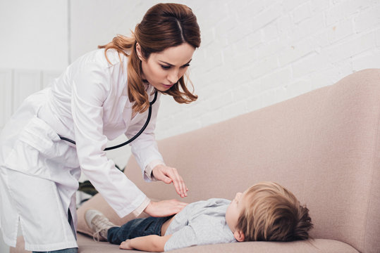 pediatrist palpating sick boy stomach on sofa in living room