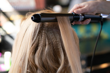 beautiful adult blonde client sits in a chair while a hairdresser master in the salon does her hair...