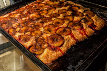 Fragrant homemade plum cake on a black baking tray, sticking out from the oven.