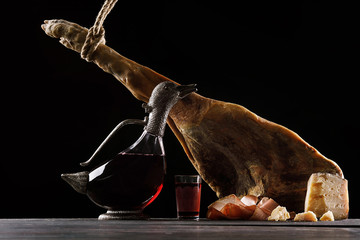 A carafe of wine in the form of a duck, a glass of wine, a leg of Parma ham and cheese. Black...