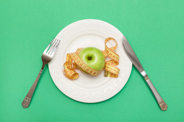Healthy lifestyle.Gym and workout concept.Flat lay of sport and diet. Top view of a plate and cutlery with an apple and a tape of centimeter on a green background