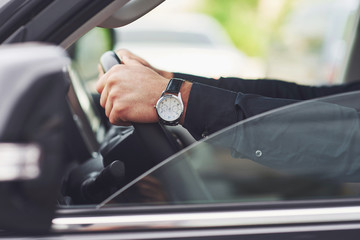 A businessman rides his car, moves on the wheel. Hand with watch.