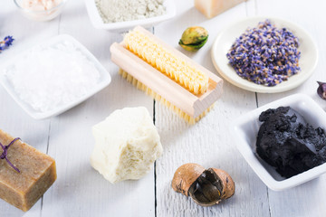 spa products: black mud and clay powder, cosmetic cream, soap, bath salt, shea butter and lavenders on white wood table background