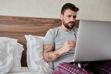 Working in hotel room. man using laptop computer while sitting in bed.