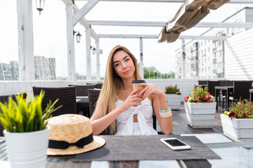 Girl in summer white dress. Sits in a cafe on veranda. Rest after work. In his hands holding a cup of hot coffee or tea. Emotionally enjoys rest in city. Business woman in city. Pending order.
