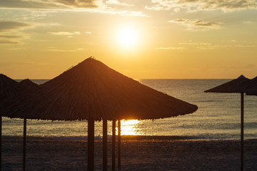 Silhouette of beach umbrellas at sunrise above the sea.