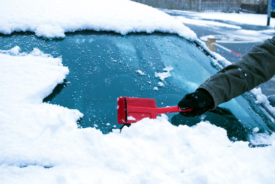 Person kehrt Schnee von Windschutzscheibe eines Autos im Winter ab, Wintereinbruch 