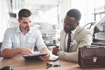 A young attractive black businessman buys a new car, he signs a contract and takes the keys to the manager