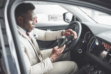 Stylish black businessman sitting behind the wheel of new luxury car. Rich african american man