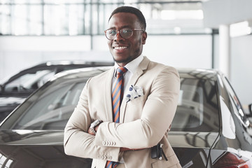 Young black businessman on auto salon background. Car sale and rent concept