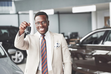 Fototapeta na wymiar The young attractive black businessman buys a new car, he holds the keys in his hand. Dreams Come True