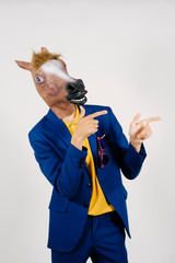 Unrecognizable man disguised with a horse head and dressed with a blue suit posing in a studio set