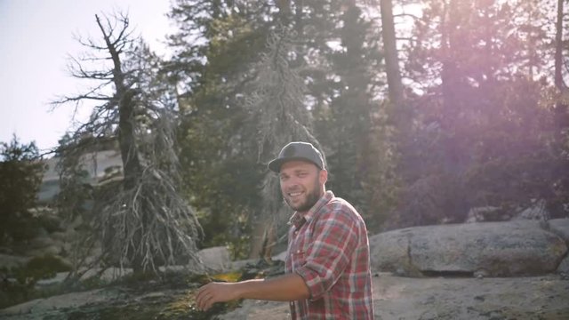 Camera follows young happy handsome man hiking alone looking at camera at beautiful Yosemite national park slow motion.