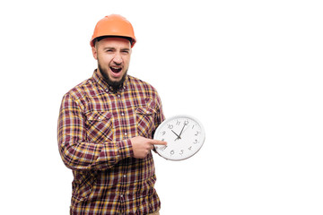 Angry Builder worker in protective construction orange helmet holding in hand a big alarm clock...