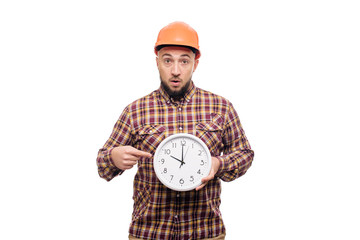 Angry Builder worker in protective construction orange helmet holding in hand a big alarm clock isolated on white background. Time to work. Building construction time.