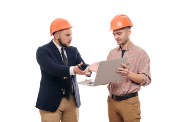 Portrait of two builders in protective orange helmets standing on white isolated background and looking at laptop display. Discuss construction project
