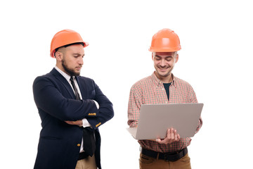 Portrait of two builders in protective orange helmets standing on white isolated background and looking at laptop display. Discuss construction project