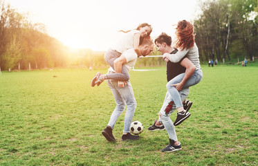 A group of friends in casual outfit play soccer in the open air. People have fun and have fun. Active rest and scenic sunset.