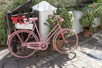 Rosa Fahrrad mit Blumen auf dem Gehweg vor dem Geschäft