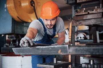 Portrait of a young worker in a hard hat at a large metalworking plant. The engineer serves the...