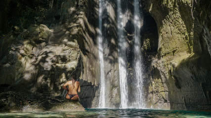 Woman in thong bikini poses in front of a beautiful and unique waterfalls