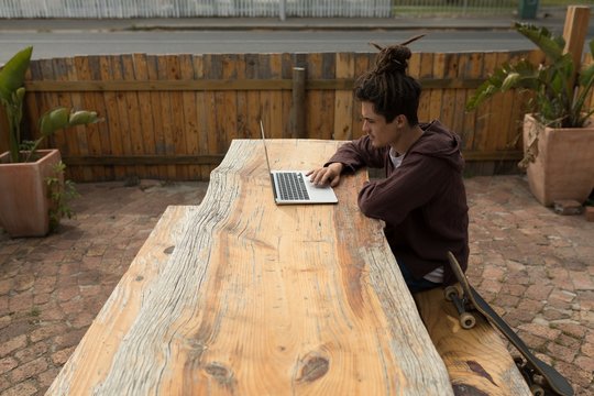 Male skateboarder using laptop at outdoor cafe