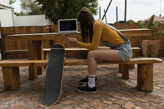 Female skateboarder using mobile phone at outdoor cafe