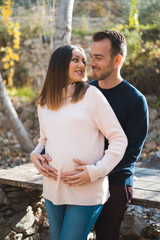 Young couple expecting baby, smiling and hugging her tummy.