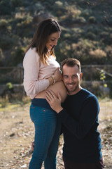 Handsome man is listening to his beautiful pregnant wife's tummy and smiling