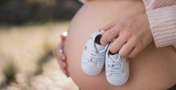 Pregnant woman outside holding baby shoes to her belly
