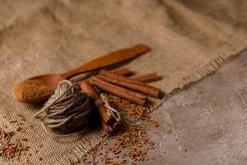 Sticks and a scattering of crushed cinnamon in a wooden spoon on textile under the burlap.