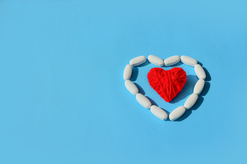 White pills capsules and red thread heart shape on blue background. Concept medical treatment,...