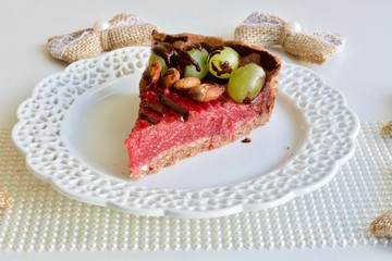 Tasty pink raspberry tart with grape and almonds on the white table.
