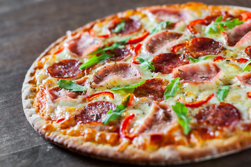 Pizza with Mozzarella cheese, ham, tomato sauce, salami, pepper, Spices and Fresh arugula. Italian pizza on wooden table background
