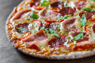 Pizza with Mozzarella cheese, ham, tomato sauce, salami, pepper, Spices and Fresh arugula. Italian pizza on wooden table background