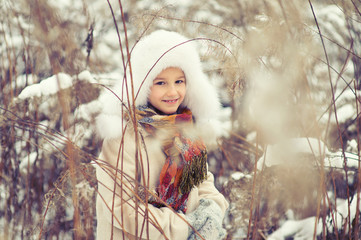 Little cute girl hide in high wet grass in snowy cold winter day playing with snowflakes