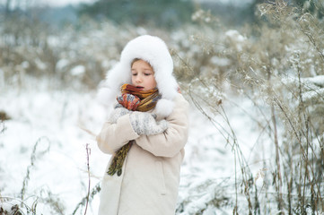 Cute toddler model girl freezing in snowy winter. Portret outside in field and park