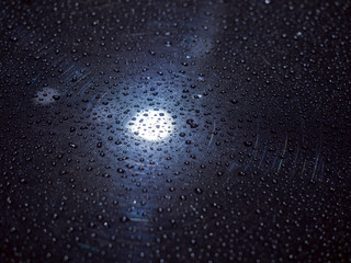 Rain drops shining on the dark blue metal surface