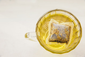 Glass cup with yellow tea with chamomile on light background
