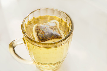 Glass cup with yellow tea with chamomile on light background