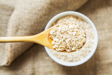 Wooden spoon and white bowl with oatmeal on light brown texxtile background