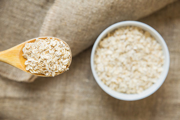 Wooden spoon and white bowl with oatmeal on light brown texxtile background