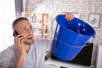 Man Collecting Water Leakage In Bucket While Calling Plumber