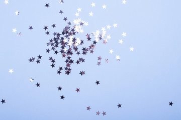 Holiday background. Group of little silver stars on blue pastel background. Top view. Copy space.